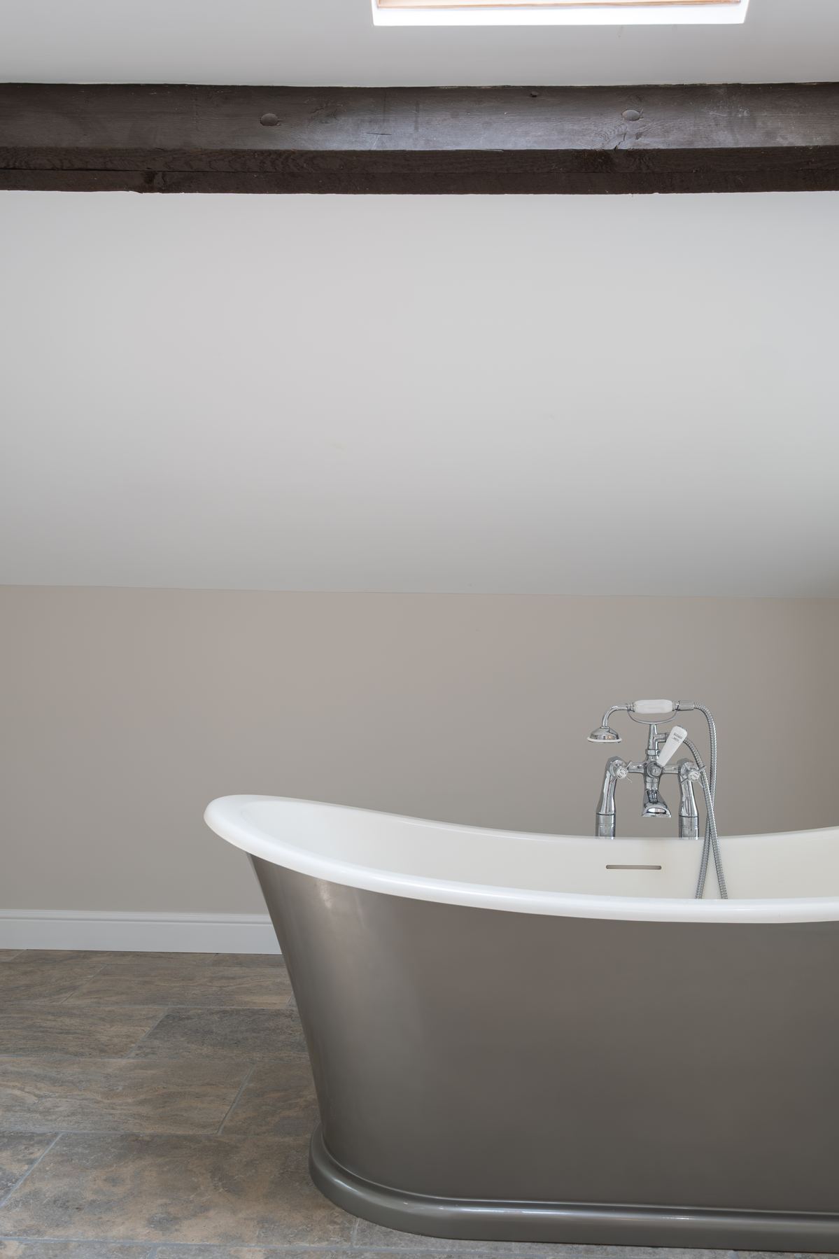 A metal-clad roll-top bath beneath an old beam and a skylight
