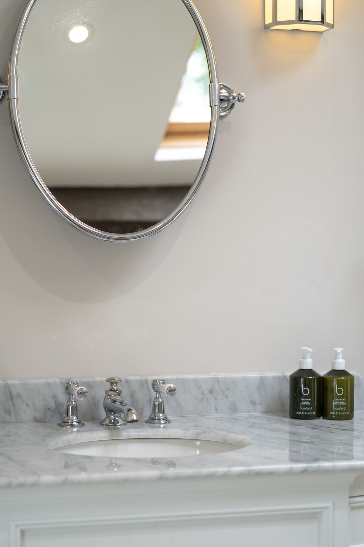 An oval chrome mirror above the marble vanity