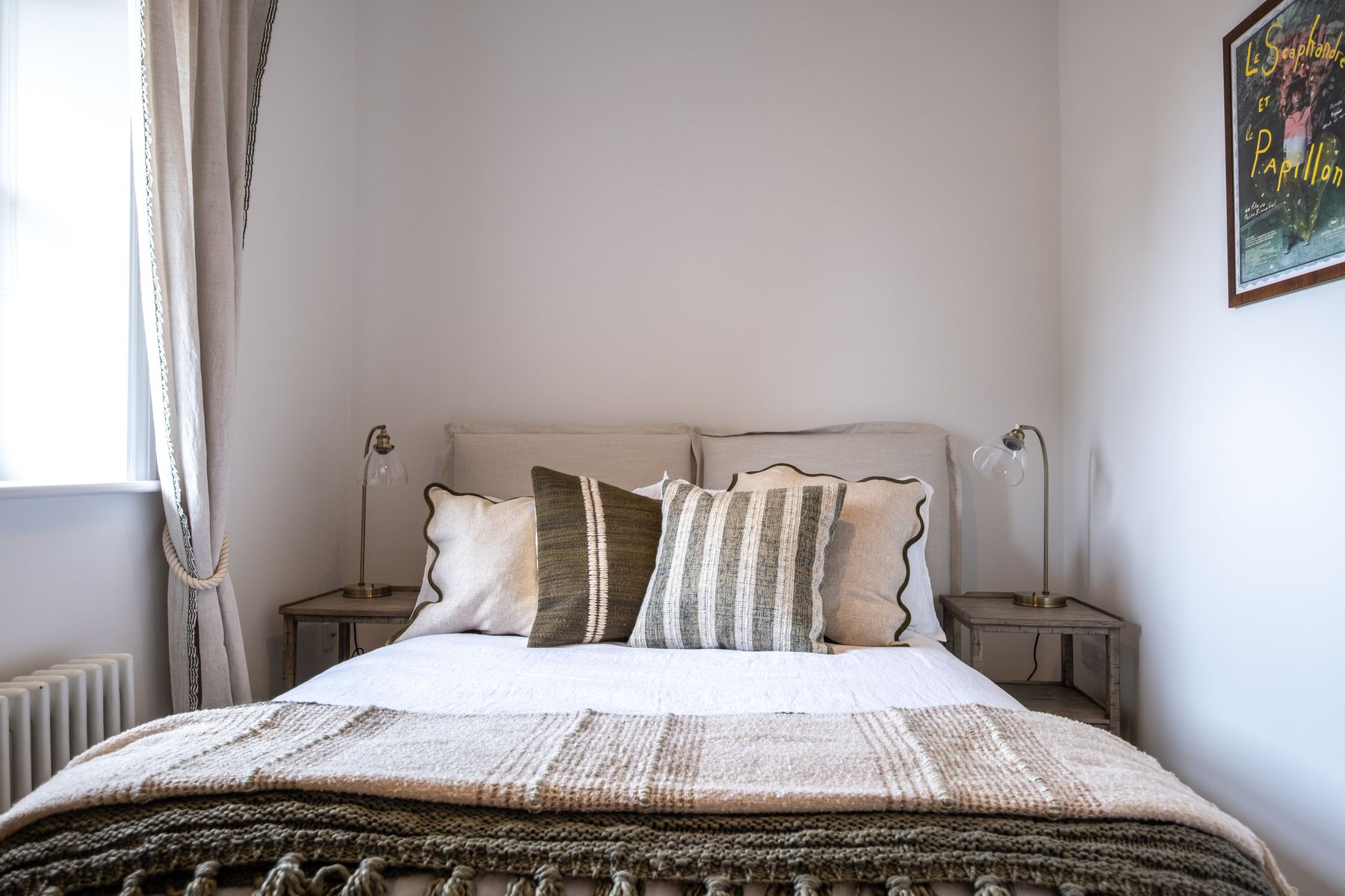 A double bedroom with linen curtains and woven cushions