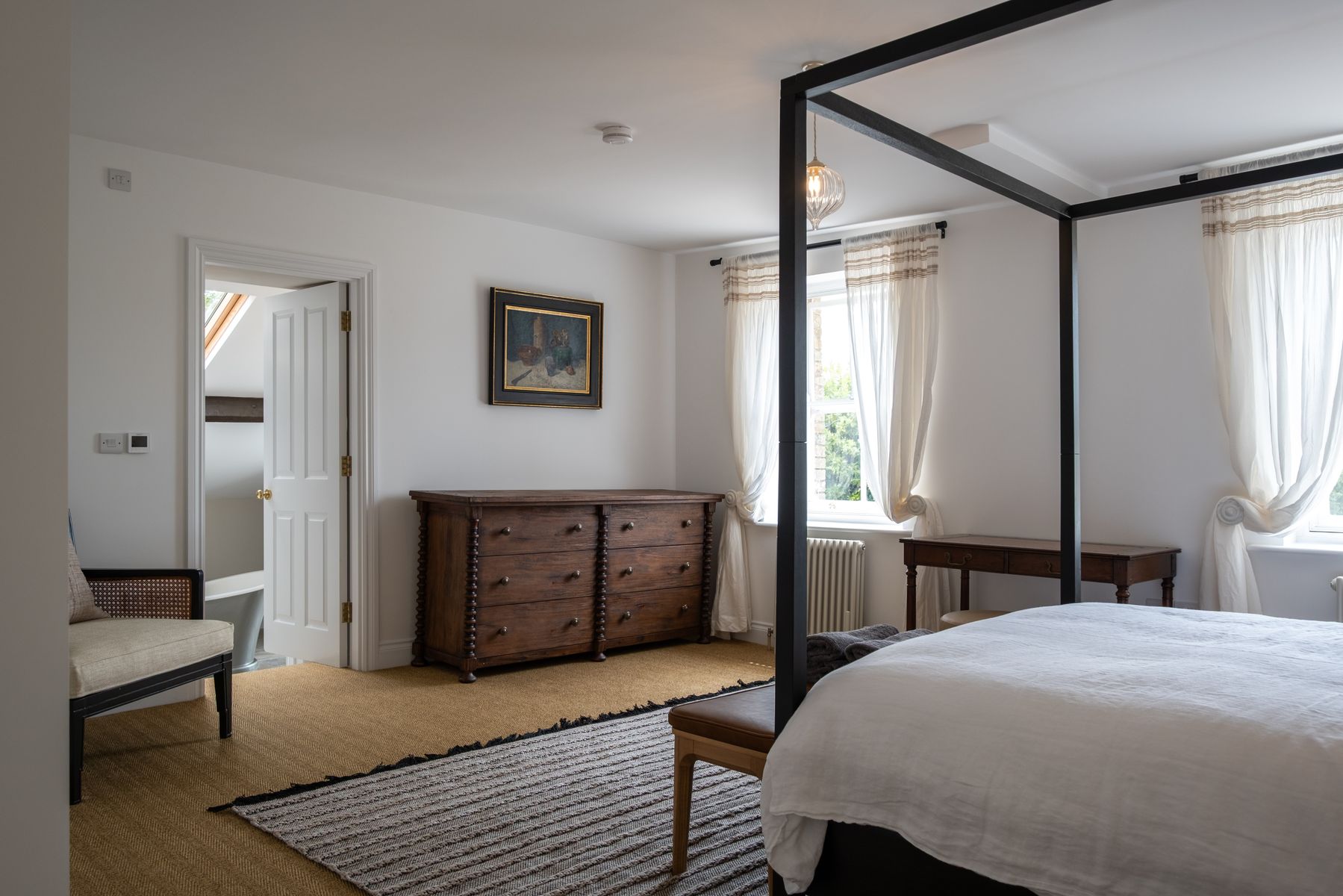 The principal bedroom, with a black four-poster bed and en suite beyond