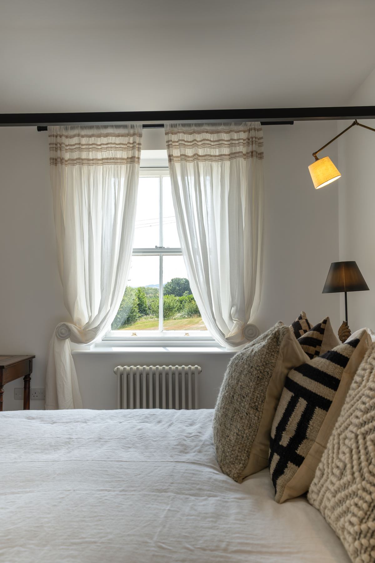 A bed made up in linen, with sheer curtains at the window