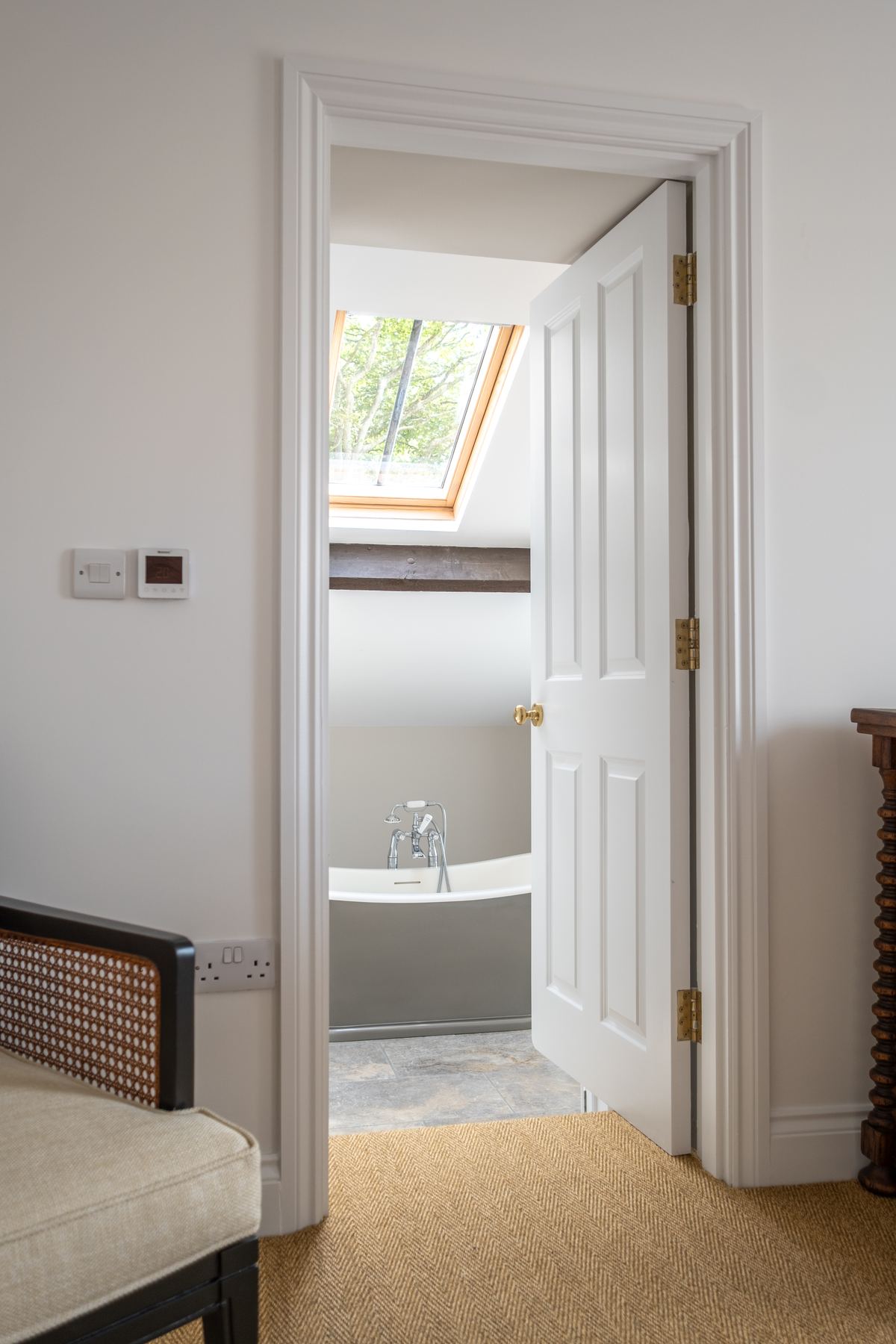 An open door through to the en suite, with a roll-top bath under the skylight