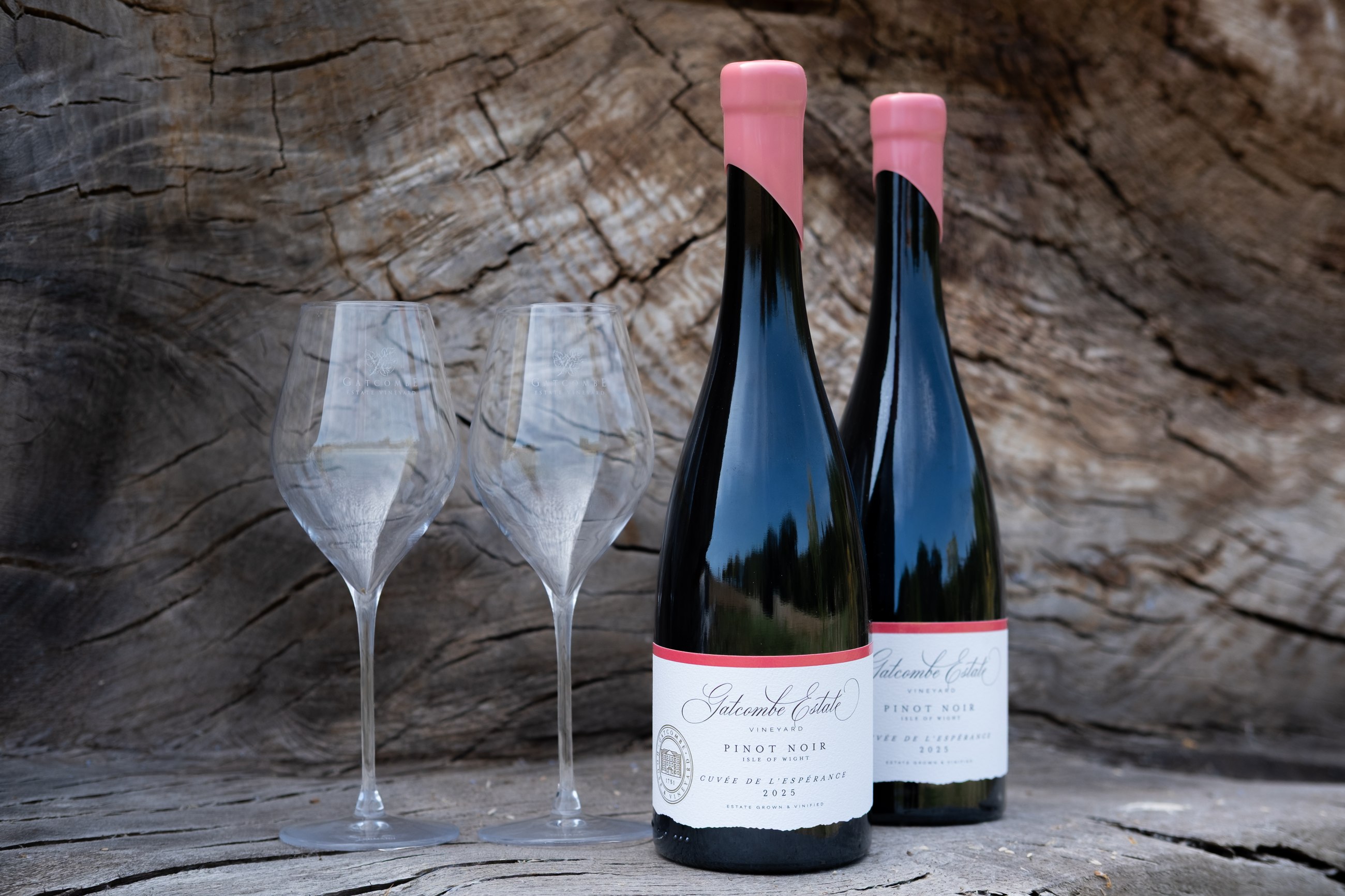 Two bottles of the estate Pinot Noir and two glasses on an old oak surface