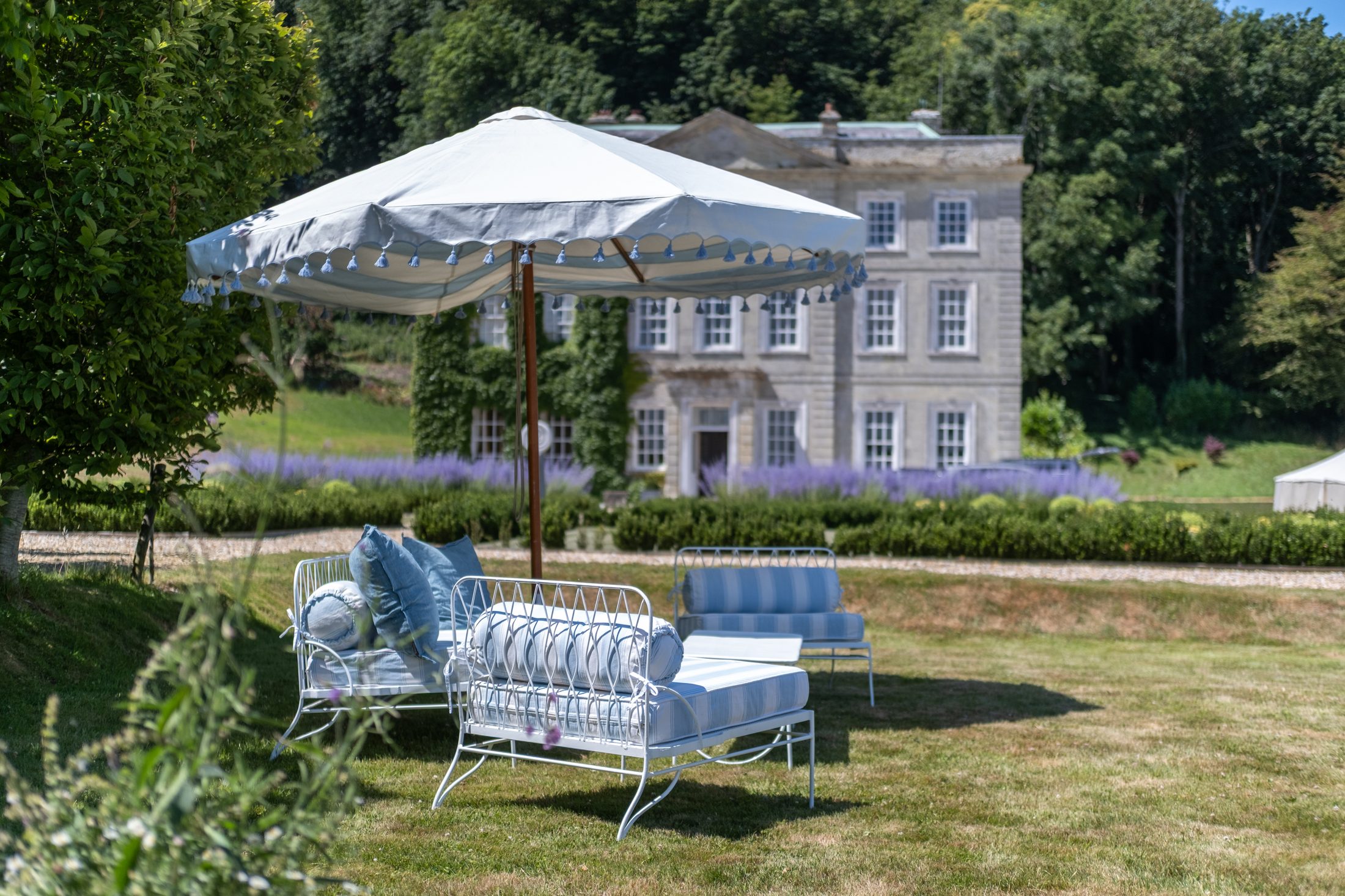 A blue-and-white tasselled parasol and day beds on the lawn, with the house behind