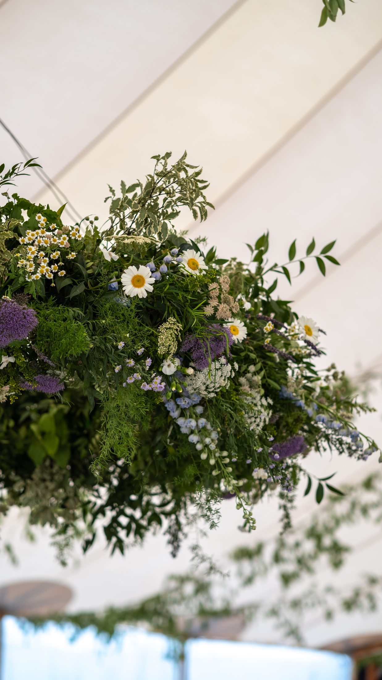 A hanging arrangement of wild flowers and greenery against the marquee canopy