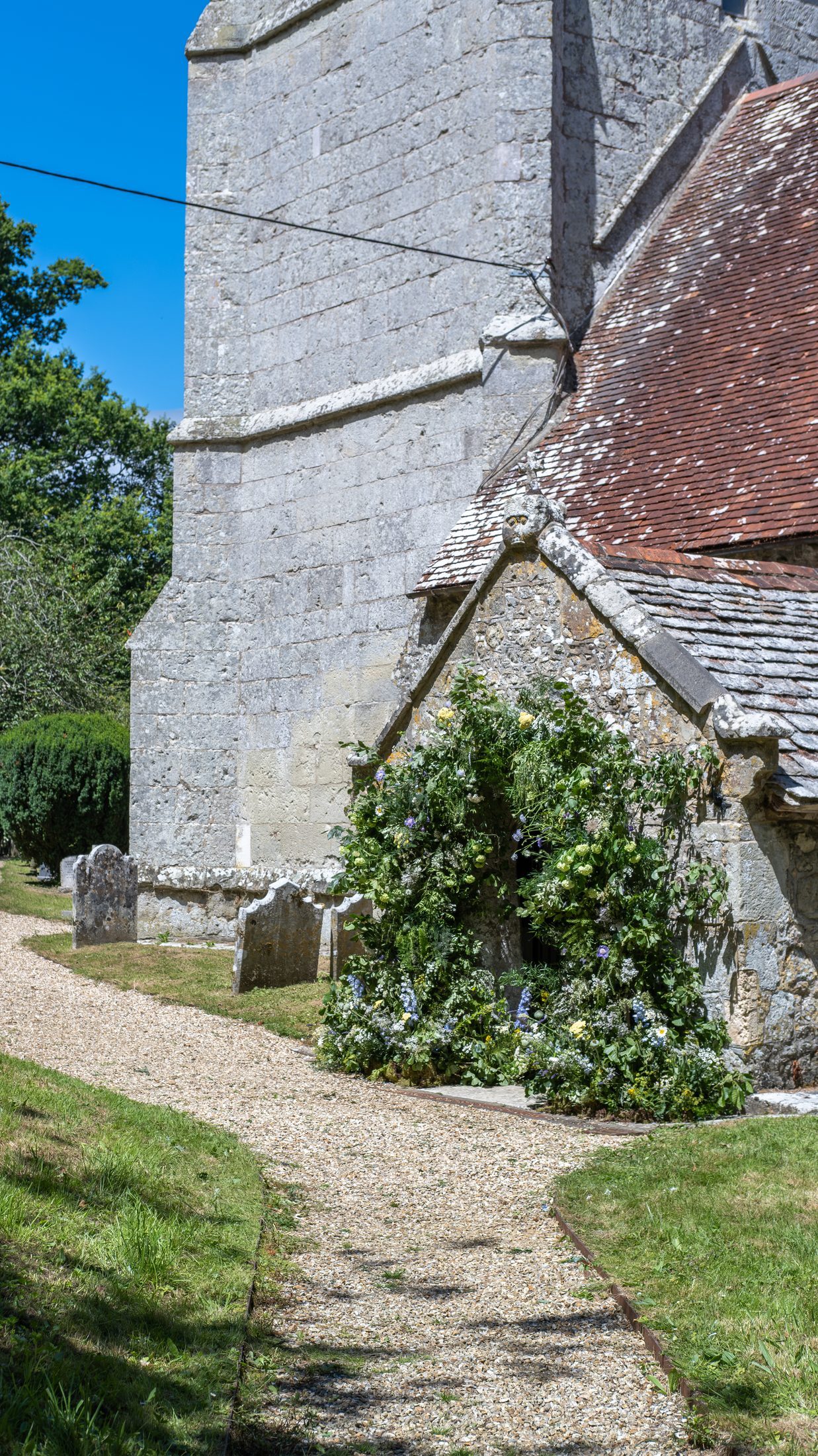 The stone tower and porch of St Olave's, with a gravel path through the churchyard
